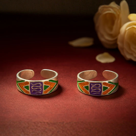 Two silver rings with colorful enameled designs on a red surface with flowers in the background.