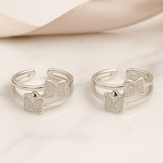 Two silver open rings with bow and paw print designs on a light background