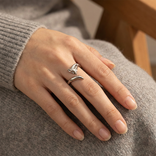 Hand wearing a silver ring with a unique design on a neutral background