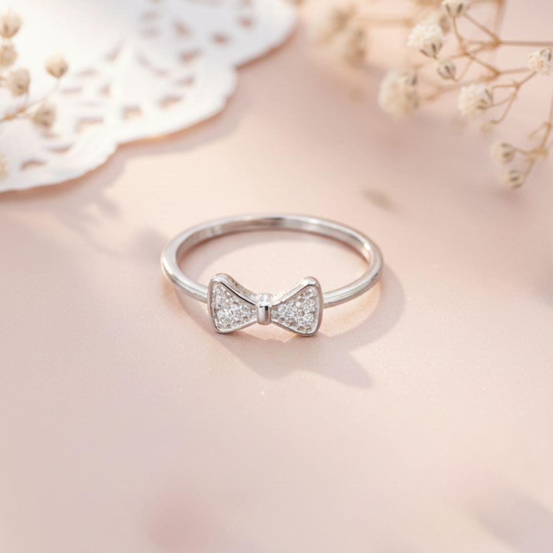 Silver ring with a bow design on a soft pink background