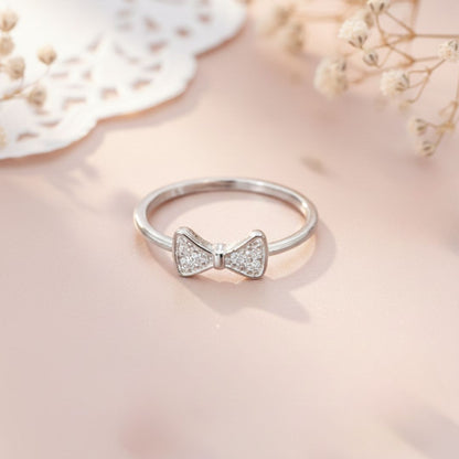 Silver ring with a bow design on a soft pink background