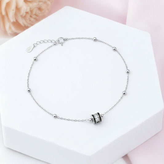 Silver bracelet with a black and white bead on a white box with a pink floral background