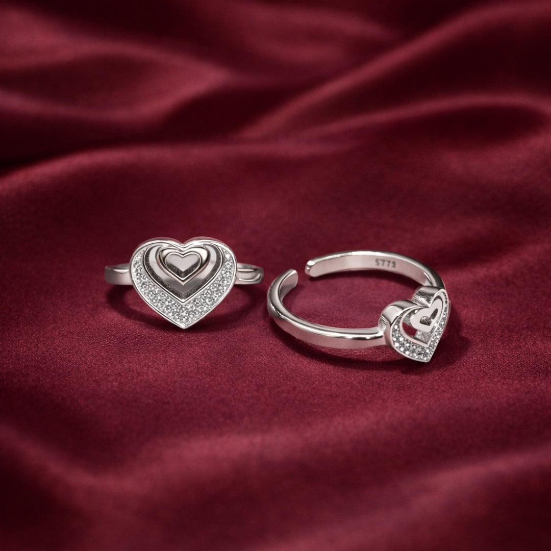 Two silver heart-shaped rings on a red fabric background