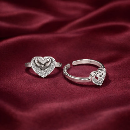 Two silver heart-shaped rings on a red fabric background