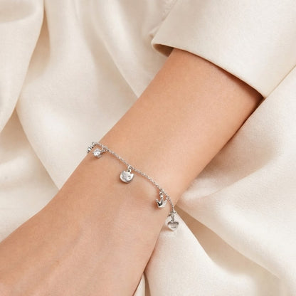 Silver bracelet with heart charms on a wrist against a soft beige background