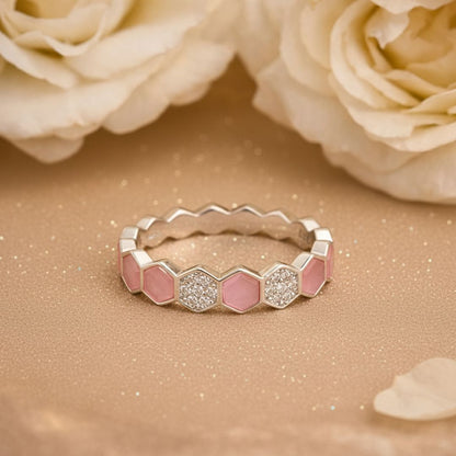 Silver ring with pink and clear gemstones on a beige surface with flowers in the background