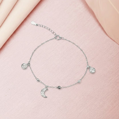 Silver bracelet with moon and star charms on a pink fabric background