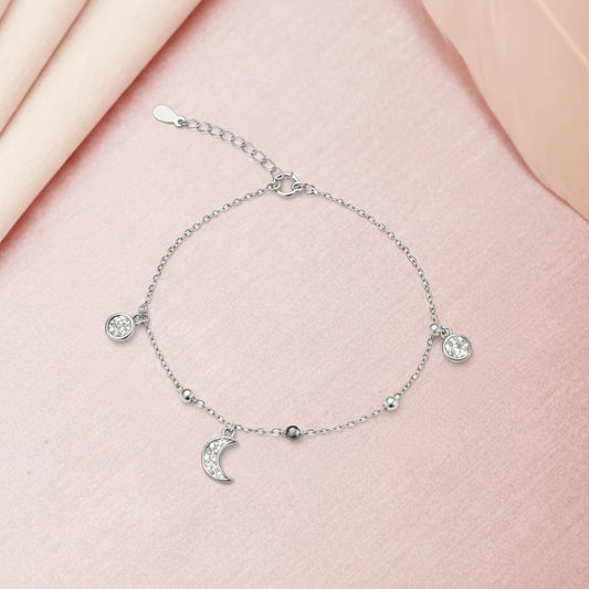 Silver bracelet with moon and star charms on a pink fabric background