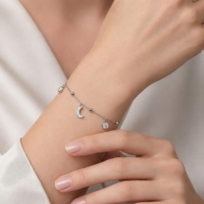 Silver bracelet with moon and star charms on a wrist against a neutral background