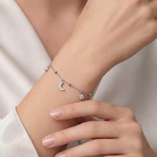 Silver bracelet with moon and star charms on a wrist against a neutral background