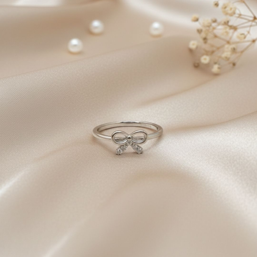 Silver bow ring on a soft beige fabric background with pearls and flowers.