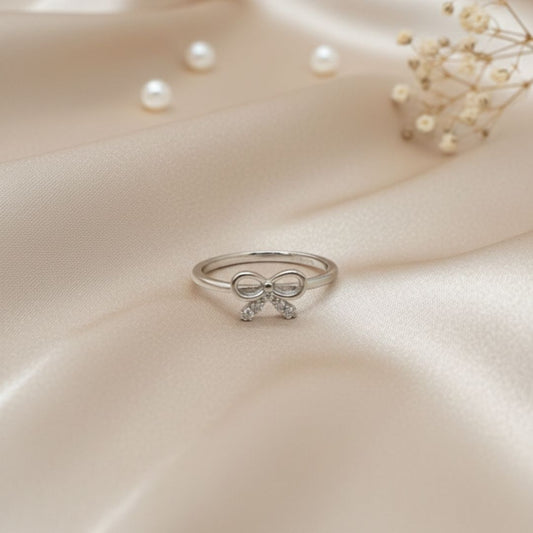 Silver bow ring on a soft beige fabric background with pearls and flowers.