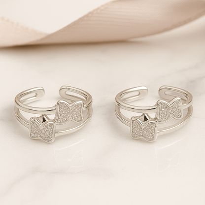 Two silver open rings with bow and paw print designs on a light background
