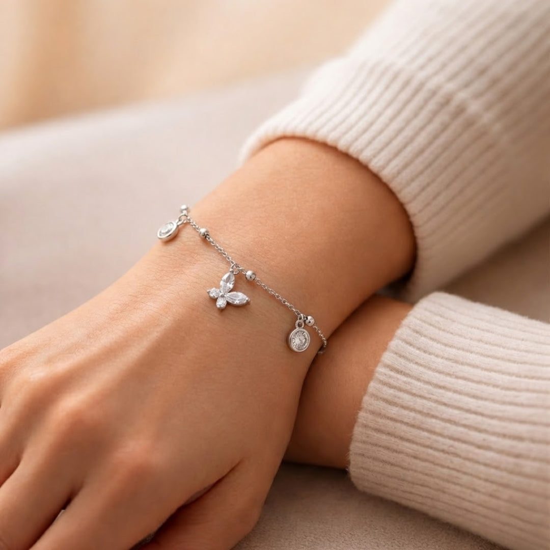 Silver bracelet with butterfly charm on a wrist against a neutral background