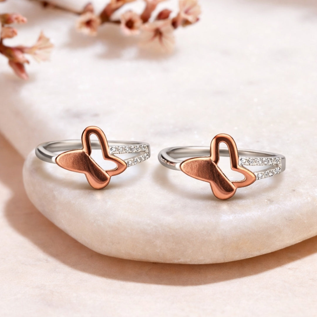 Butterfly-shaped silver and rose gold rings on a stone surface with floral background