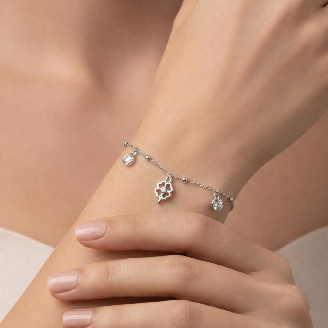Silver bracelet with charms on a wrist against a neutral background