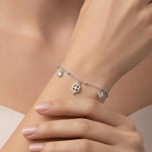 Silver bracelet with charms on a wrist against a neutral background