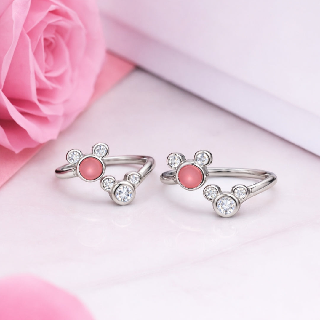 Two silver rings with pink stones on a pink surface with a pink rose.