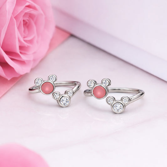 Two silver toe rings with pink stones on a pink surface with a pink rose.