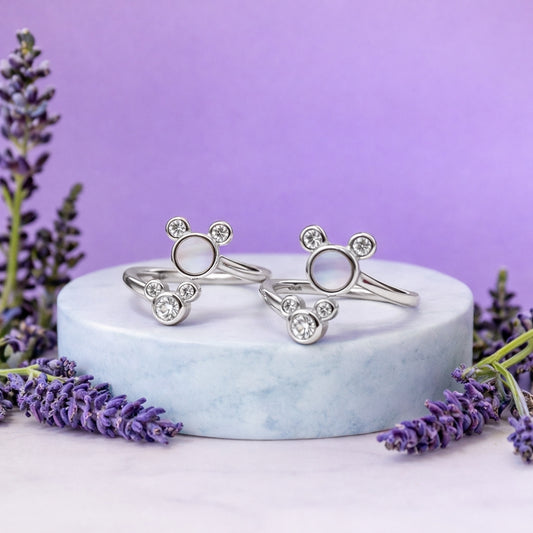 Silver toe rings with gemstones on a white marble stand against a purple background with lavender flowers.