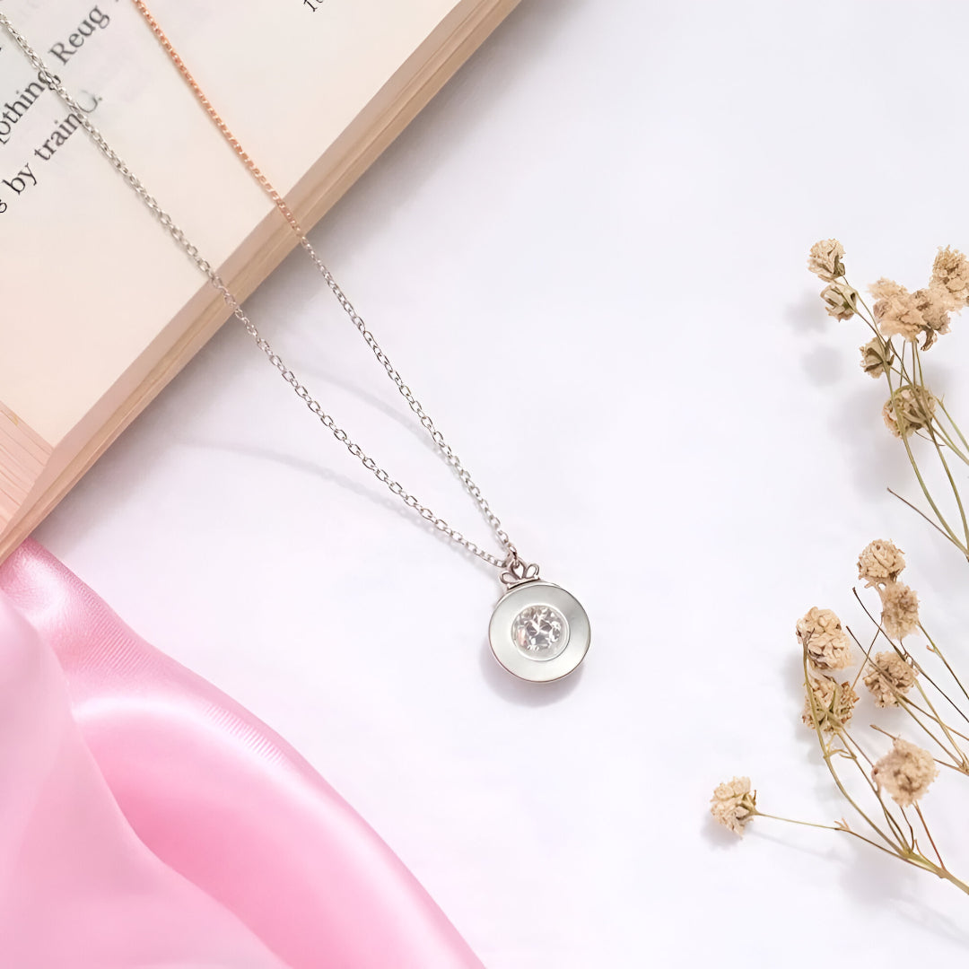 Necklace with a circular pendant on a white surface with dried flowers and a pink object.