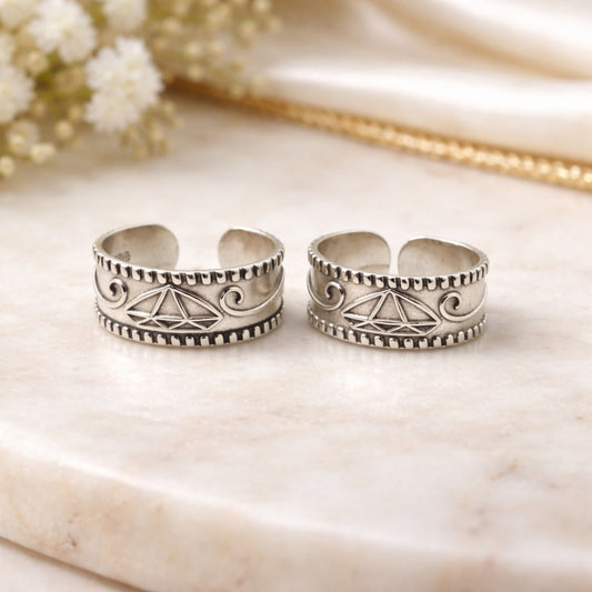 Two silver toe rings with intricate designs on a marble surface.