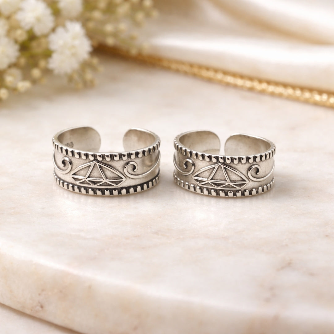 Two silver toe rings with intricate designs on a marble surface.