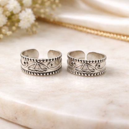 Two silver toe rings with intricate designs on a marble surface.