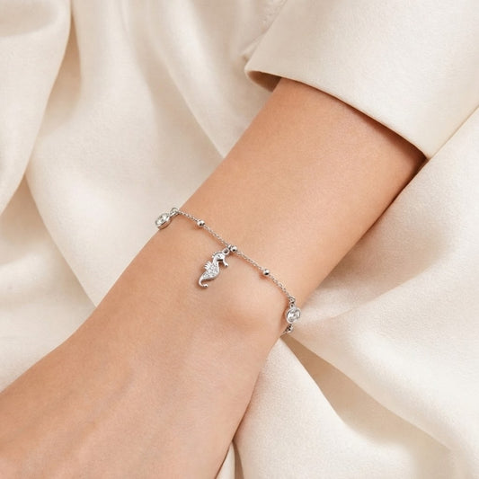 Silver bracelet with a horse charm on a wrist against a beige fabric background