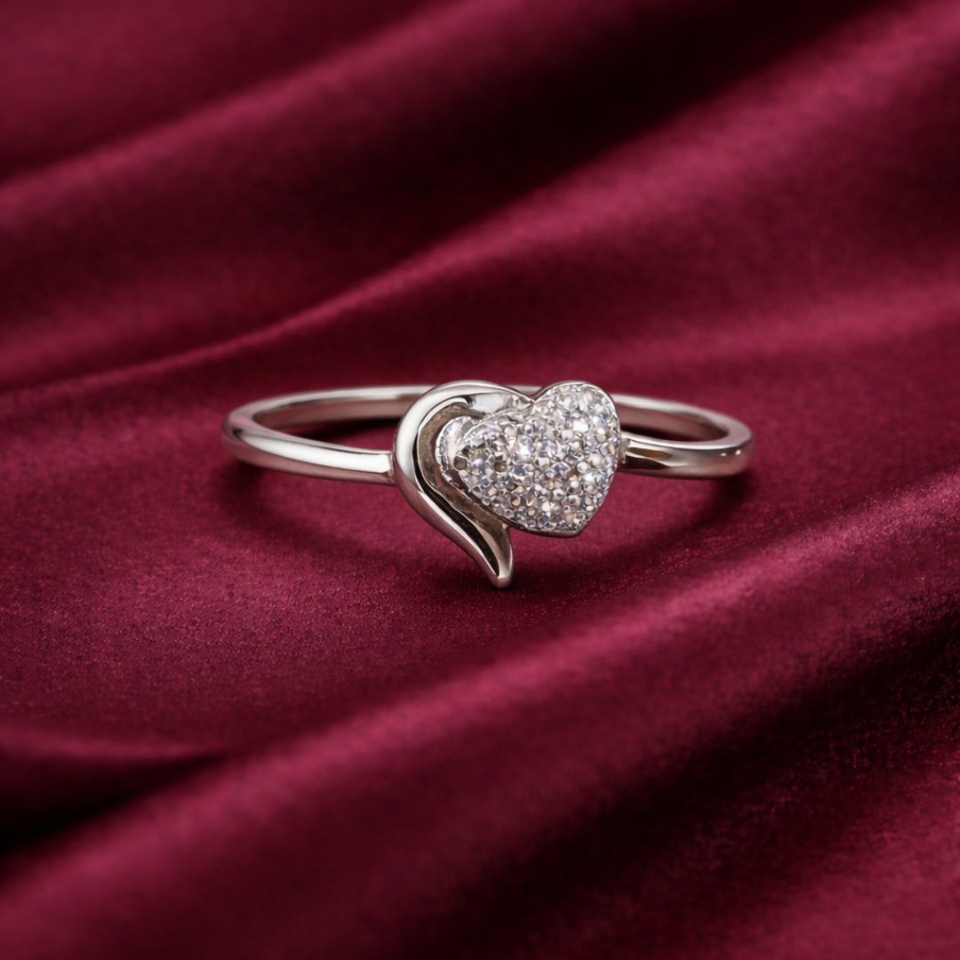 Silver heart-shaped ring with embedded stones on a burgundy fabric background