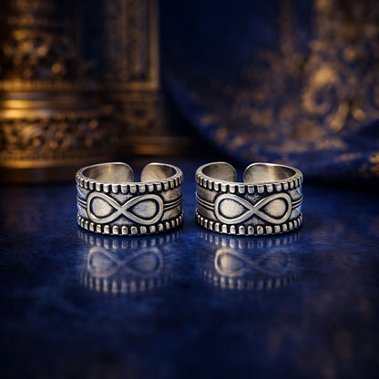 Two silver infinity symbol rings on a reflective blue surface with ornate background