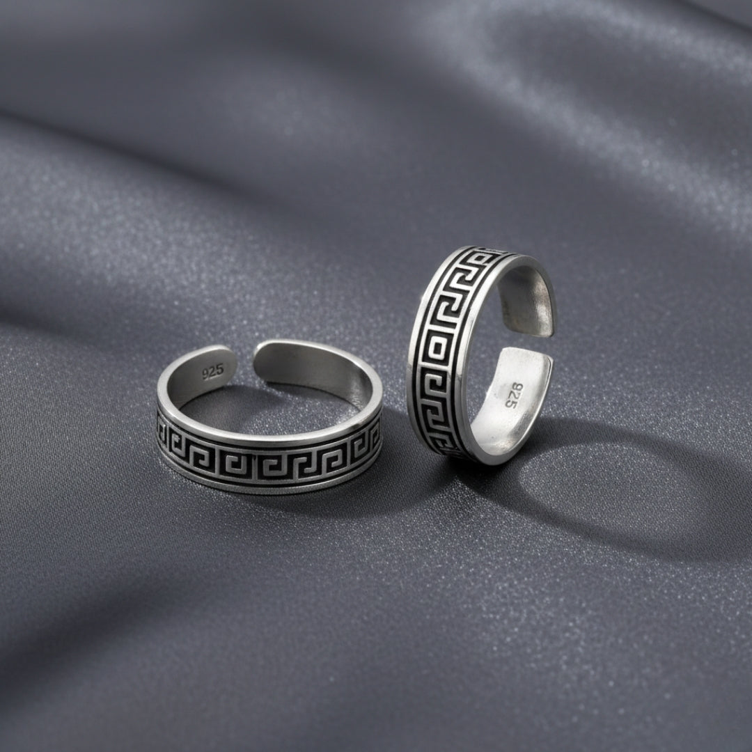 Two silver rings with Greek key design on a gray fabric background