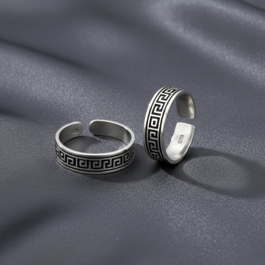 Two silver rings with Greek key design on a gray fabric background