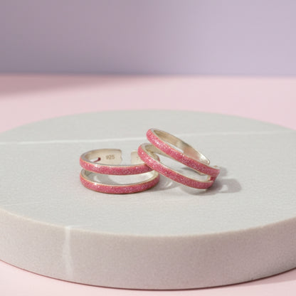 Three pink glittery rings on a round white platform with a light purple background