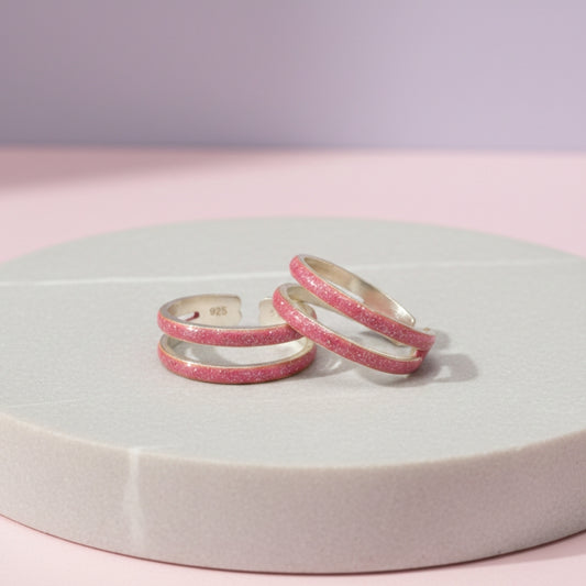 Three pink glittery rings on a round white platform with a light purple background