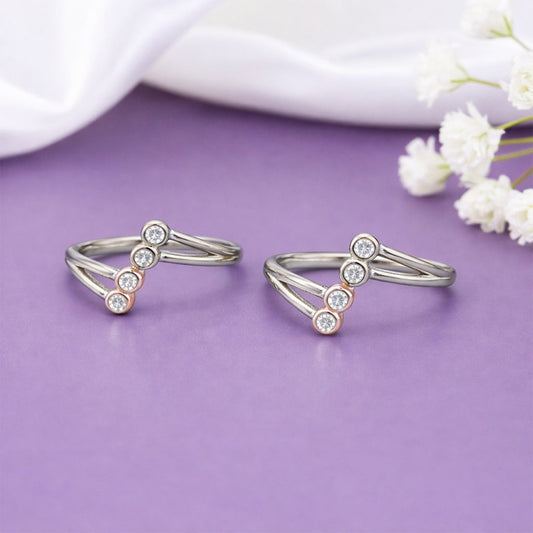 Two silver toe rings with small stones on a purple surface with white flowers.
