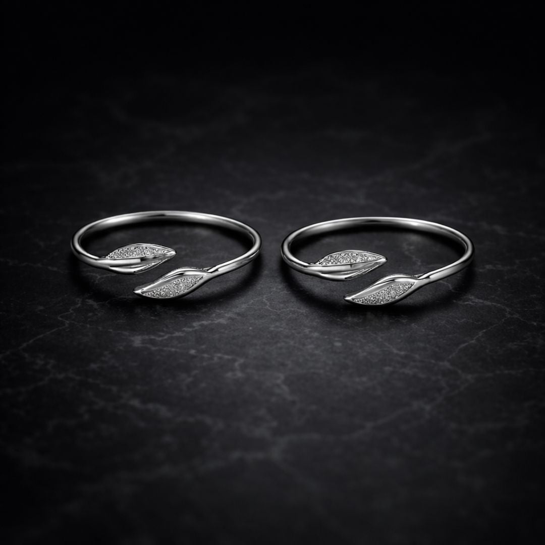 Two silver rings with leaf designs on a dark textured surface