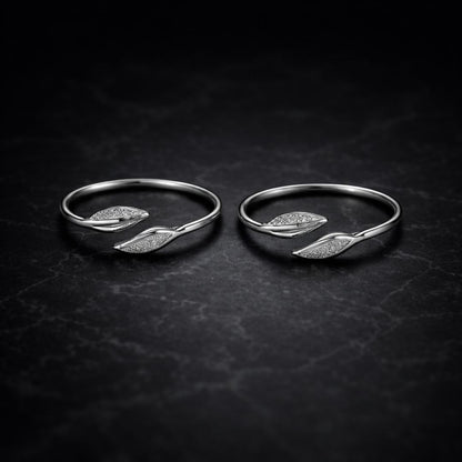 Two silver rings with leaf designs on a dark textured surface