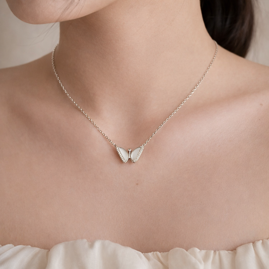 Silver butterfly necklace on a person wearing a white top