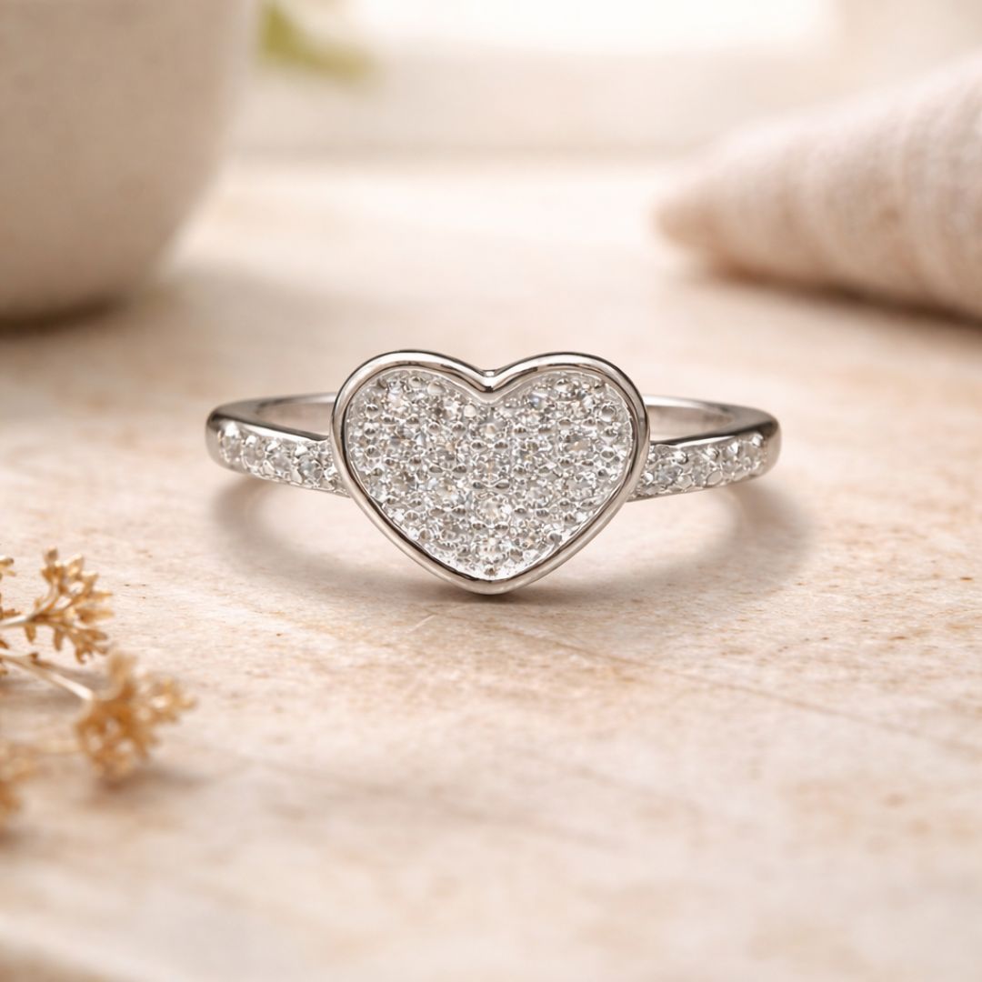 Heart-shaped silver ring with sparkling stones on a soft beige background