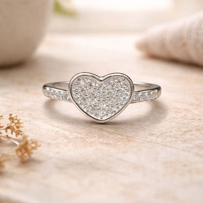 Heart-shaped silver ring with sparkling stones on a soft beige background