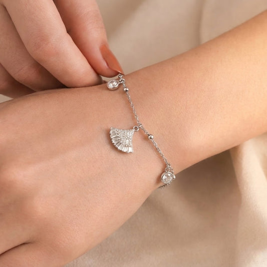 Silver bracelet with fan-shaped charm on a wrist against a neutral background