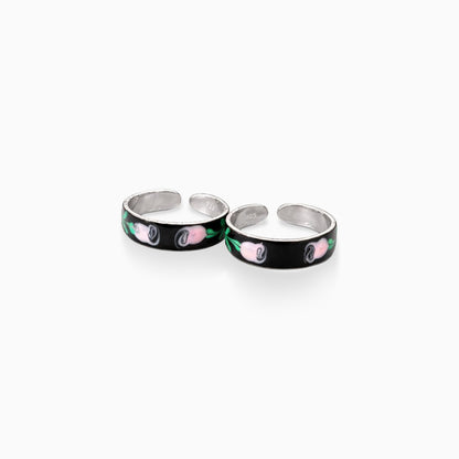 Two silver rings with black bands featuring pink and green designs on a white background