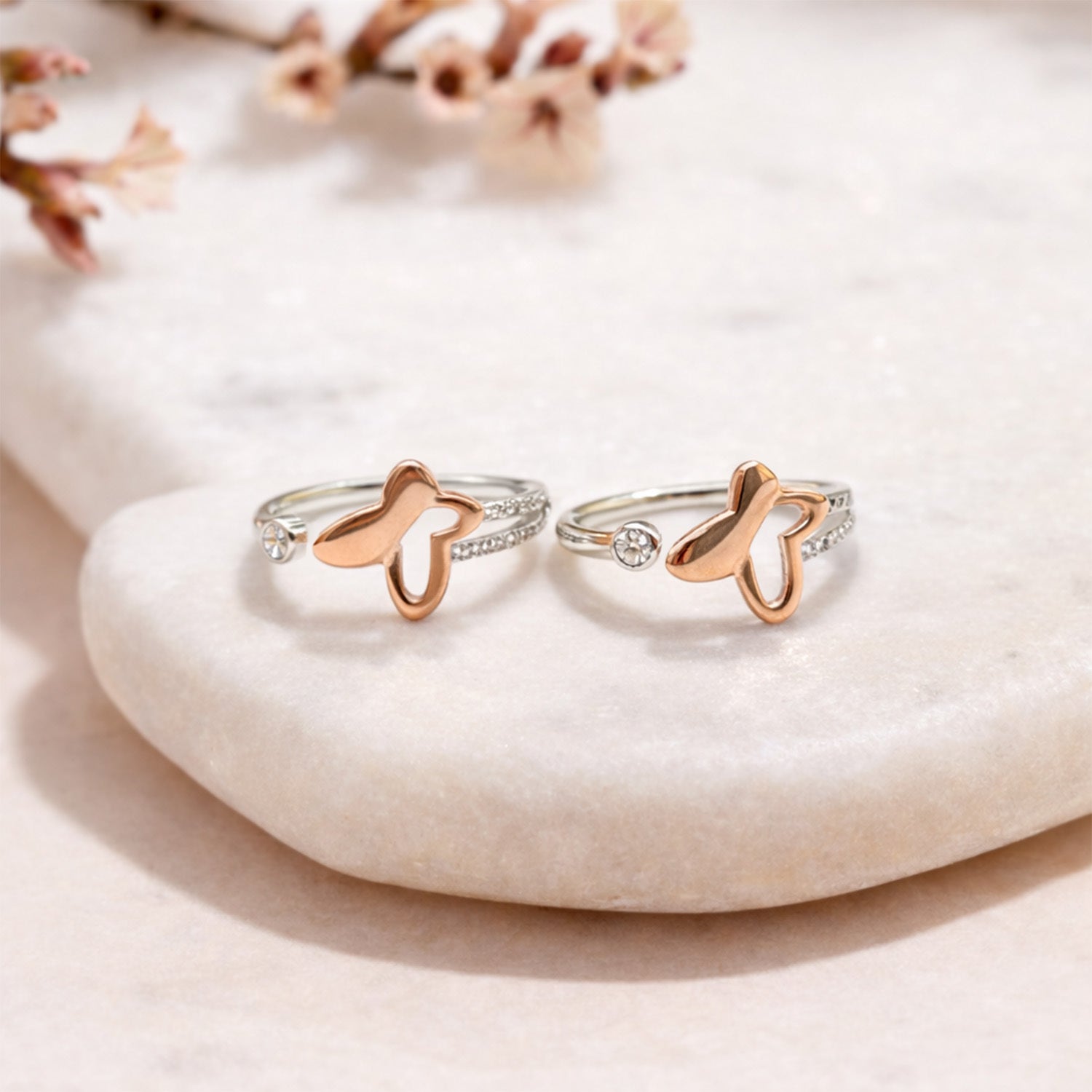 Two rose gold butterfly rings/ toe rings on a white stone surface with a soft background