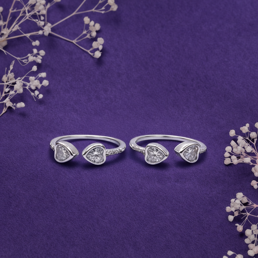 Two silver heart-shaped rings with clear stones on a purple background with dried flowers.