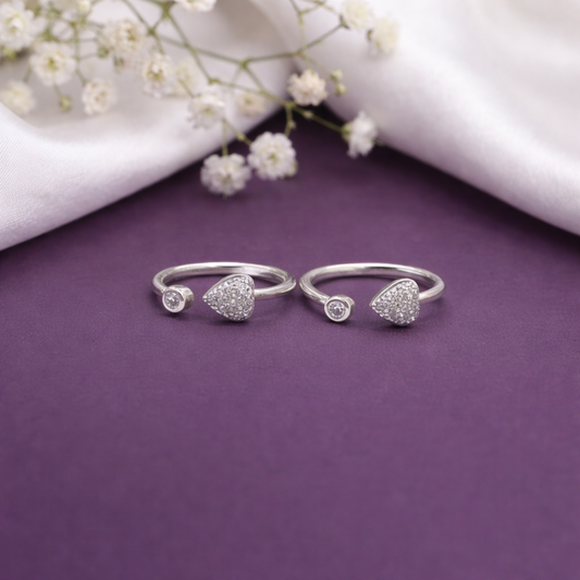 Two silver heart-shaped rings on a purple surface with white flowers in the background