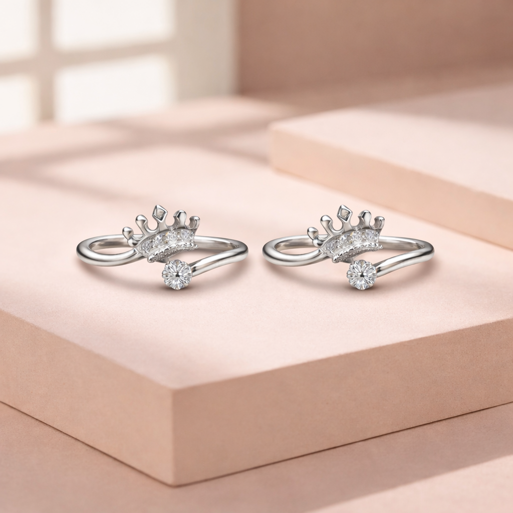 Pair of silver crown shaped rings with diamond accents on a light pink surface