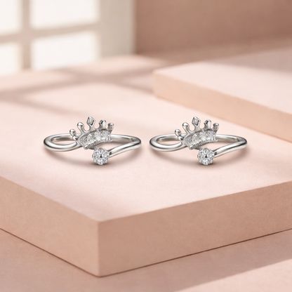 Pair of silver crown shaped rings with diamond accents on a light pink surface