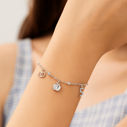 Silver bracelet with charms on a person's wrist against a neutral background