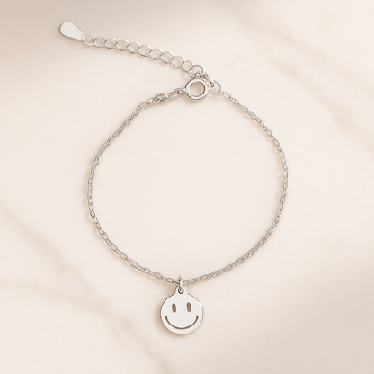 Silver bracelet with a smiley face charm on a beige background